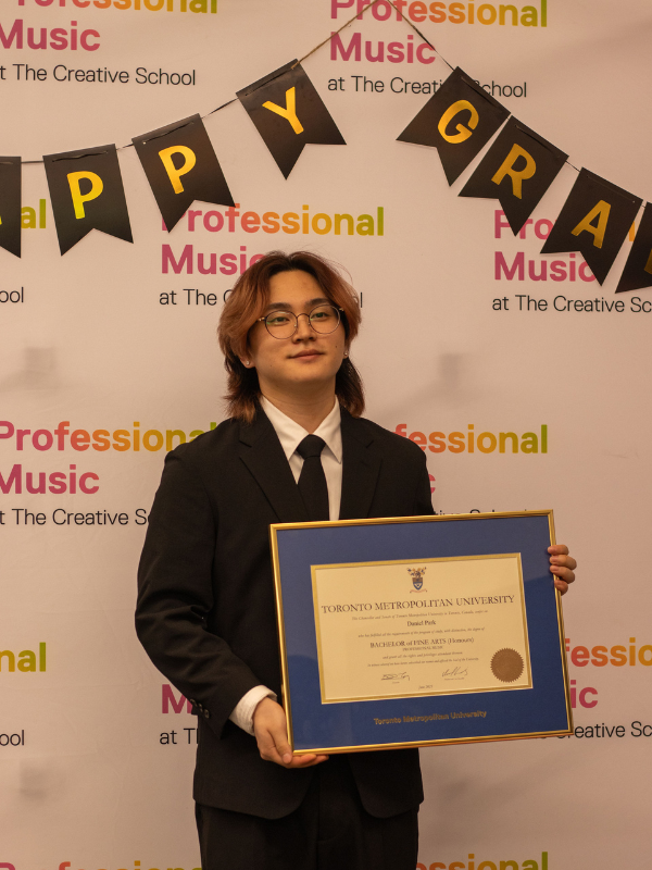 A Professional Music student holding up their certificate and smiling at the camera. 